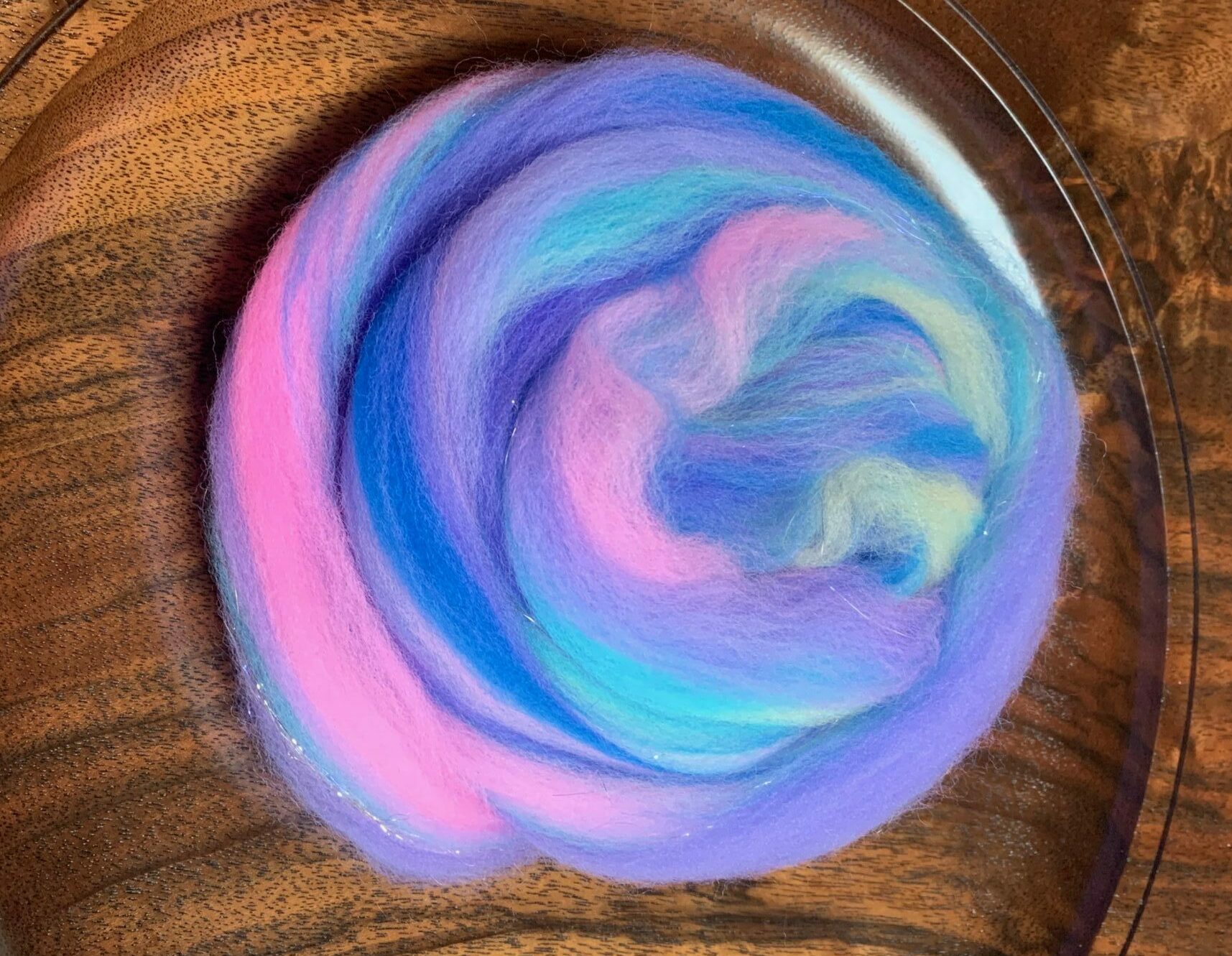 A nest (roving that's been coiled up until it looks like a nest) of the fiber described in the previous image. It's now a blend, so you can see repeating streaks of each color. It's set on a wooden platter that my partner made.