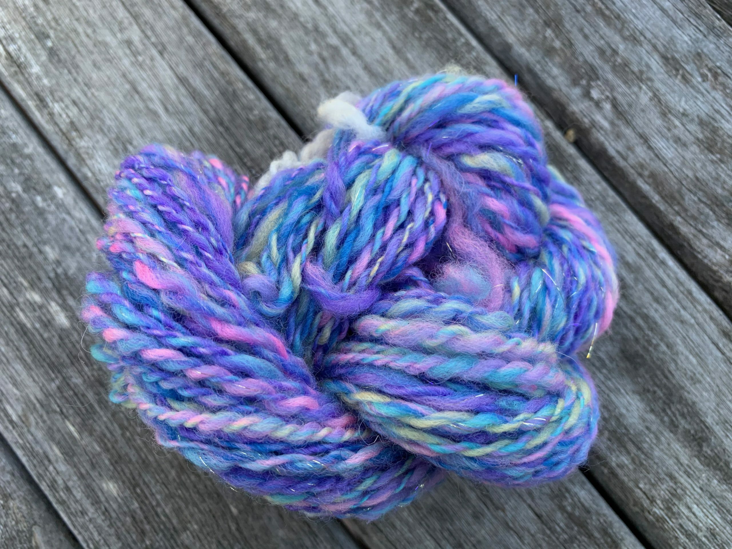 The same fiber, now all spun up and plied, then wound into a skein and twisted into something of a pretzel. It has all the same colors, and they make a barber-pole effect because each ply has many colors in it, and the two plies together usually bring different colors together.